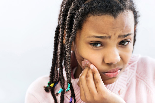 Young girl holding her cheek due to a tooth ache