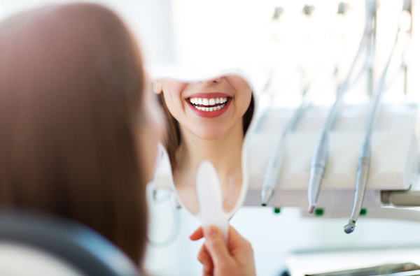 Woman looking at her smile in a mirror at Irvine Dentistry.