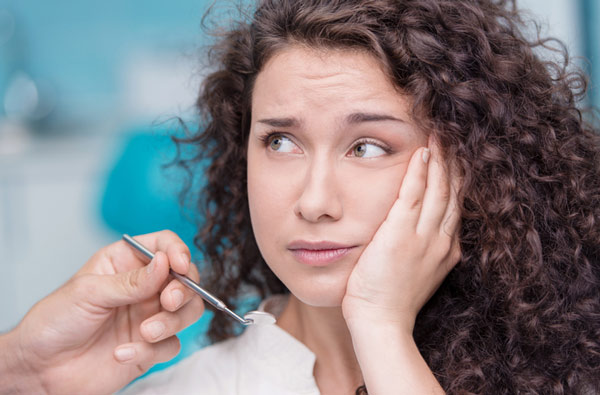 Woman holding cheek due to tooth ache at Irvine Dentistry in Irvine, California.